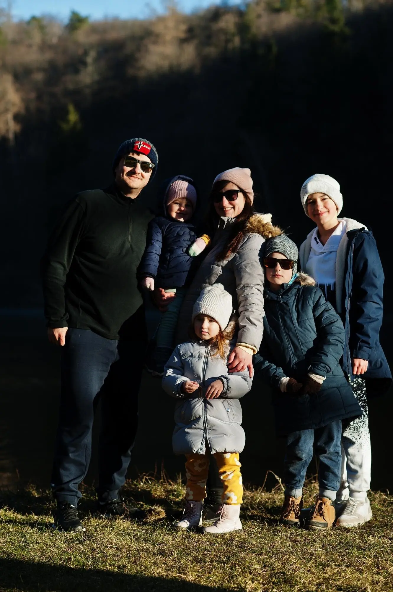 Große Familie mit vier Kindern an einem Teich in einem Park im frühen Frühjahr.